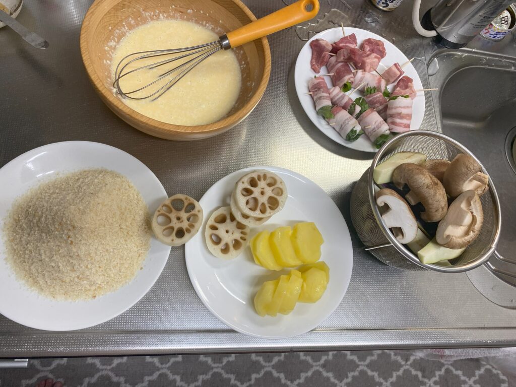 バッター液、揚げる前の豚シソ巻き、一口豚肉、シイタケ、なず、ジャガイモ、レンコン、パン粉が用意されている
