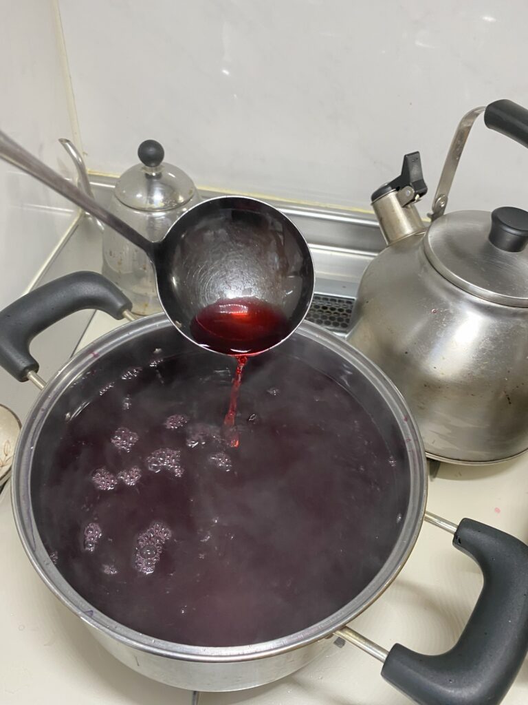鍋の中の赤紫蘇ジュースをお玉ですくっています。